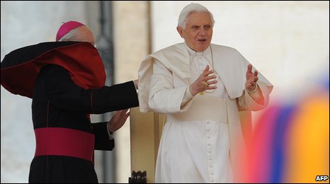 A bishop adjusts the robe of Pope Benedict XVI (R) during his weekly audience in St Peter square at the Vatican on April 14, 2010
